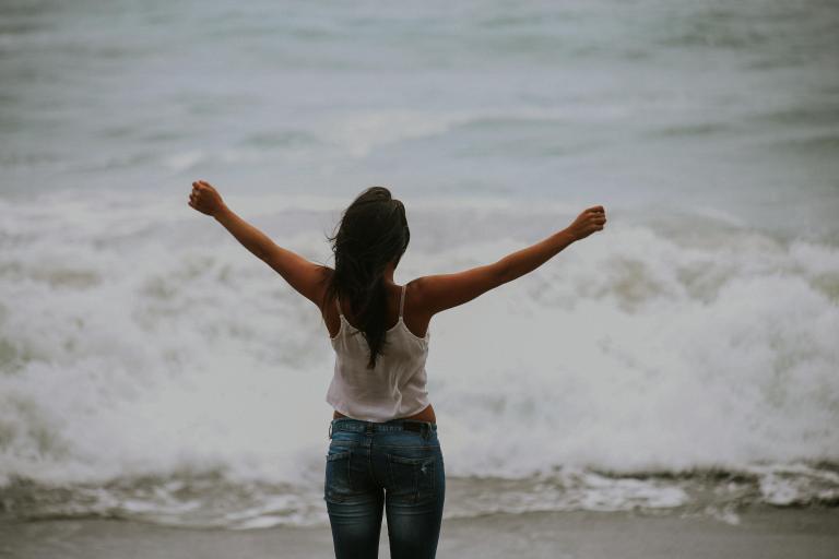 Woman with stretched arms in front of the ocean