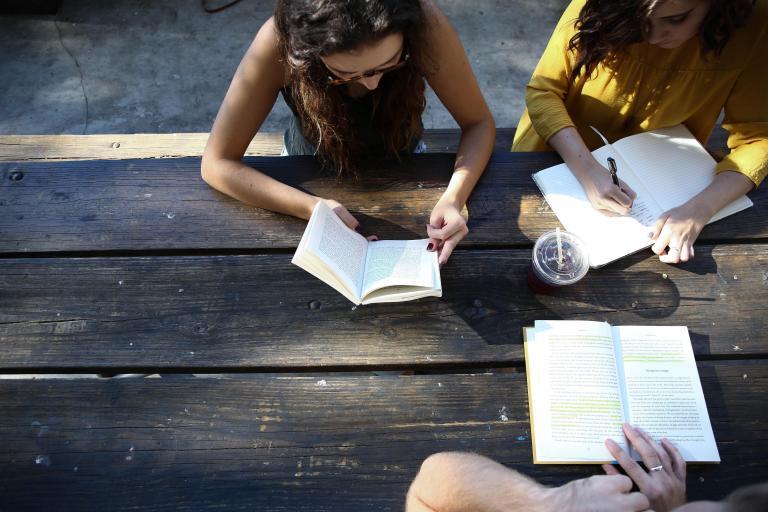 People sitting at a table and reading books outside